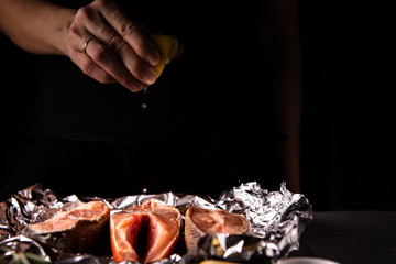cook squeezes lemon juice on a salmon dish with ingredients for cooking on a table on a black background
