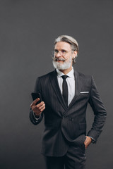 Business and fashionable bearded mature man in a gray suit smiling and talking by phone on the grey background.