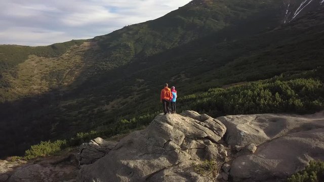 Aerial view of a hikers man and his child son climbing together on a big rock in mountains.