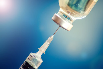 A bottle with vaccine and syringe in front of blue background. Medicine, science and healthcare concept