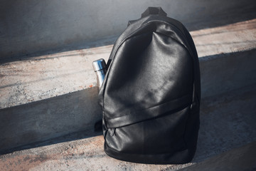 Black backpack with reusable steel thermo water bottle inside on urban stairs.