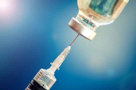 A bottle with vaccine and syringe in front of blue background. Medicine, science and healthcare concept