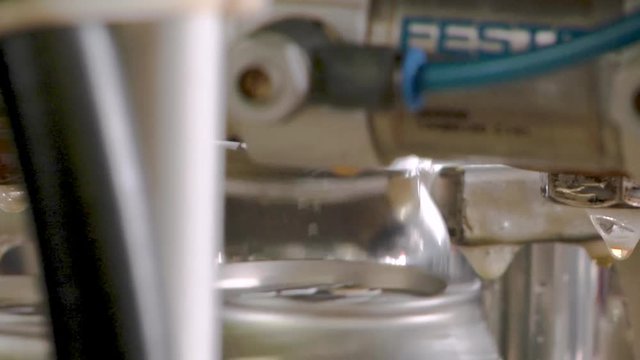 Full beer cans having the lids sealed onto the cans on a canning conveyor belt line in a production brewery. Extreme close up.