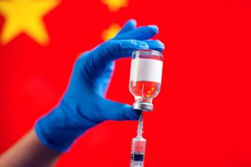 A doctor holding a bottle with vaccine and syringe in front of flag of China. Coronavirus, epidemic and healthcare concept