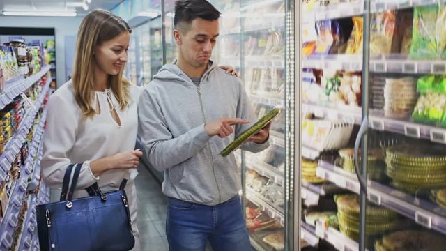 Portrait of young woman and man buying frozen pizza at grocery store