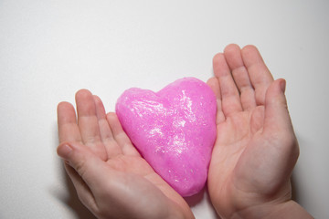 Fototapeta premium The child's hands hold a slime in the form of a pink heart. Concept. Valentine's day.