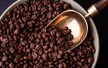 Coffee theme. Plate with coffee beans on black wooden table. Vintage spoon.