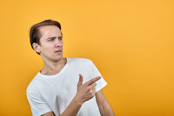 Cute man with white t-shirt surprised shows direction of finger or points to object