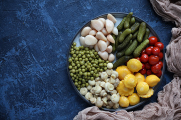 Fermented food in a plate on a white textural wooden table. Cucumbers, garlic, mashrooms, tomatoes, green peas, patissons, champignons. National Russian food pickles in brine close up and copy space