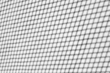Gray shadow of a metal mesh on a white wall. Abstract background.