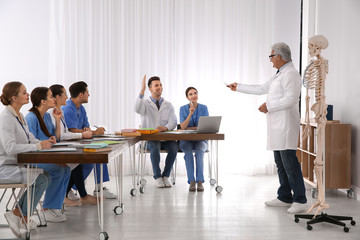Medical students and professor studying human skeleton anatomy in classroom