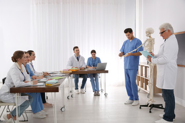 Medical students and professor studying human skeleton anatomy in classroom