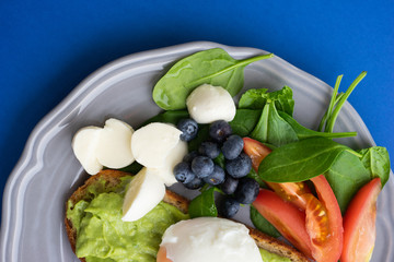 Wholesome tasty full of vitamins and health breakfast with avocado, berries, cheese and tomatoes with basil.