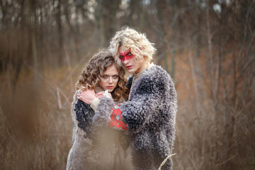 Young attractive man with curly blond hair with an ethnic ritual pattern on his face and ethnic clothes of the East European Slavs hugs his girlfriend a bride