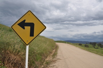 country gravel road with a left turn sign