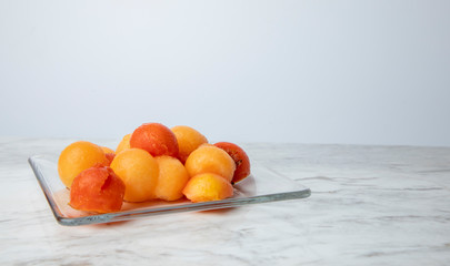 Bolitas de fruta en un plato de cristal, sobre una barra de mármol blanco con una cuchara y el...