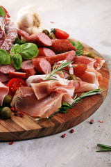 Food tray with delicious salami, pieces of sliced prosciutto crudo, sausage and basil. Meat platter