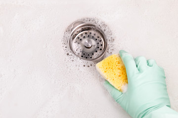 Person hand holding a yellow sponge, cleaning acrylic sink in light green gloves in the kitchen,...