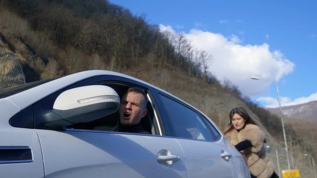 two beautiful girls push the broken car on the road. a man sits behind the wheel