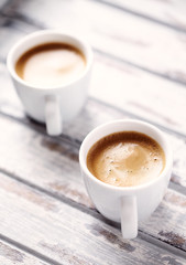 Two cups of coffee on bright wooden background.