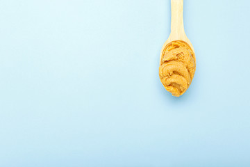 Flat lay wooden spoon with creamy peanut butter with copy space on blue colored background. Flat lay with place for text for peanut butter, peanut paste. Vegan food concept.