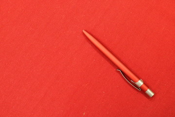 A red ballpoint pen with silver hardware sits on a red textile background on the right. Mobile photo.  