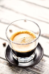 Coffee in glass cup on bright wooden background. Close up.