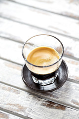 Coffee in glass cup on bright wooden background.