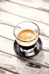 Coffee in glass cup on bright wooden background. 