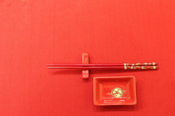A red and gold ceramic set of sushi and roll dishes is placed in the lower right corner on a red cloth background. 