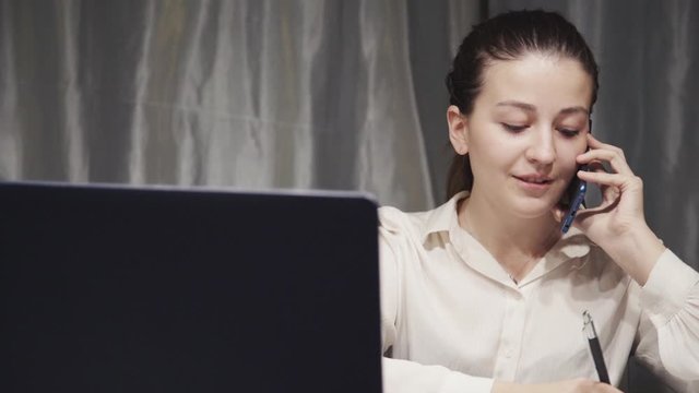 Young manager woman using laptop answering call and writing client request on paper. office worker consulting a customer while checking informaion on computer. operator work concept.