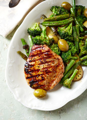Grilled Turkey Breast with oven baked broccoli and green olives. Bright wooden background. Top view. 