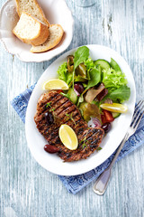 Grilled steak with fresh salad on bright wooden background. Top view. 
