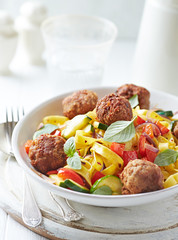 Tagliatelle pasta with meatballs, red pepper and zucchini. Bright background.