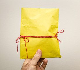 Man hand holding against white background beautifully packaged in linen wrapping paper yellow gift present for the upcoming birthday valentine new year christmas Hanukkah black friday holiday - Powered by Adobe