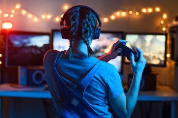 Games online, a young girl playing computer games using a joystick or a gamepad. On three large monitors, creative light. Strategies, racing and gaming business © Anton