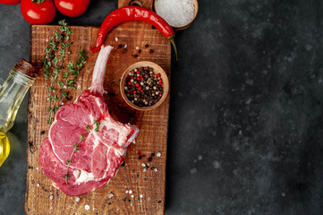 raw beef steak, beef tomahawk with spices, tomatoes, sunflower oil, thyme on a stone background....
