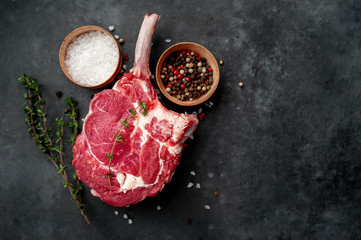 raw beef steak, beef tomahawk with spices,  thyme on a stone background. with copy space for your...