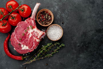raw beef steak, beef tomahawk with spices, tomatoes, thyme on a stone background. with copy space for your text