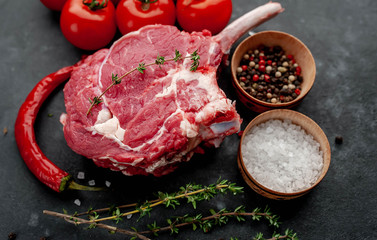 raw beef steak, beef tomahawk with spices, thyme on a stone background.