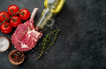raw beef steak, beef tomahawk with spices, tomatoes, sunflower oil, thyme on a stone background. with copy space for your text
