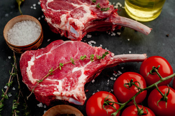 two raw steaks, beef tomahawk with spices and thyme on a stone background.