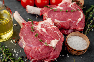 two raw steaks, beef tomahawk with spices and thyme on a stone background.