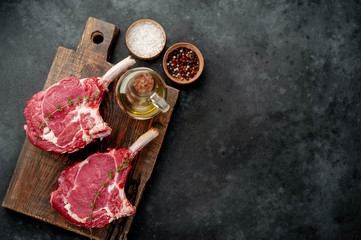 two raw steaks, beef tomahawk with spices, thyme on a stone background. with copy space for your text