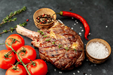 grilled beef steak - tomahawk with spices, tomatoes, thyme on a stone background.