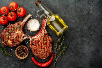 Obraz na płótnie Canvas two grilled beef steak - tomahawk with spices, tomatoes, sunflower oil on a stone background. with copy space for your text