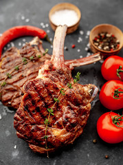 two steaks - grilled beef tomahawk with spices, tomatoes, red pepper on a stone background.