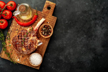 grilled beef steak - tomahawk with spices, tomatoes, thyme on a stone background. with copy space for your text