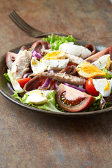 Salad with hard-boiled eggs, tomatoes, lettuce, red onion and mackerel on rustic background.