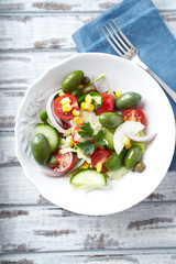 Healthy salad with green olives, sweet corn, cherry tomatoes, red onion, baby spinach, capers and fresh herbs. Bright wooden background. Top view.